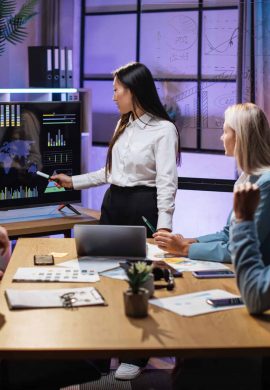 Asian woman pointing on monitor with financial report during conference with multiracial partners. Business colleagues gathering at office room for brainstorming.